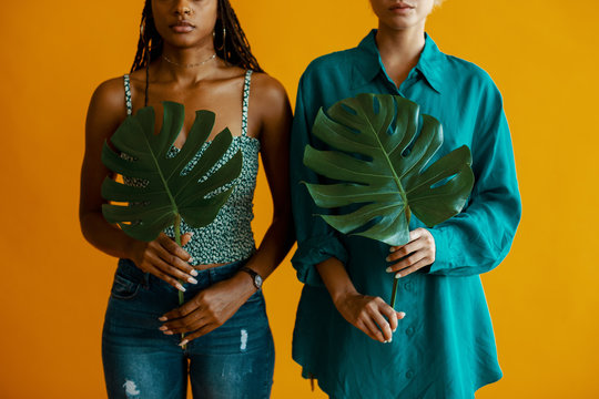 Two women hold monstera leaves