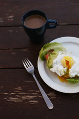 Close-up flat lay of delicious poached egg with liquid yolk on toast with fresh salad leaves and avocado at dark rustic brown wooden background/ table. Top view of healthy protein breakfast or lunch. 