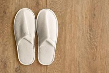 Top view of a pair of new soft white slippers in the hotel on wooden floor. A pair white slippers, Isolated on wooden floor. Top view.  
