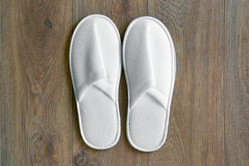 Top view of a pair of new soft white slippers in the hotel on wooden floor. A pair white slippers, Isolated on wooden floor. Top view.  
