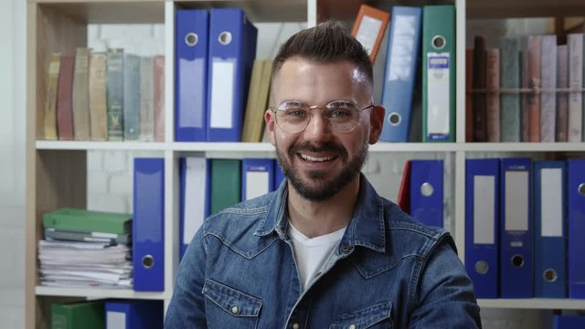Portrait of pleased nice-looking hipster smiling cheerfully enjoying break time sitting working in modern company office. People occupation.