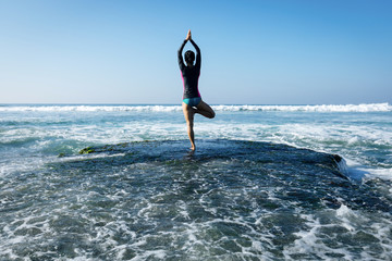 Woman practice yoga at seaside cliff edge facing the coming strong sea waves