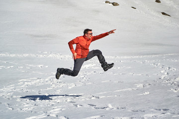 Fototapeta na wymiar Man jumping in a funny pose, high above the snow, on a sunny Winter day.