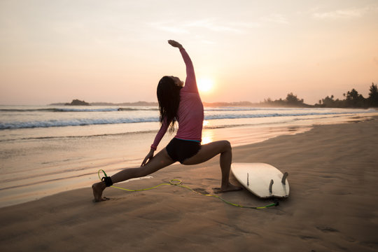 Woman surfer warming up on sunset beach. - Powered by Adobe