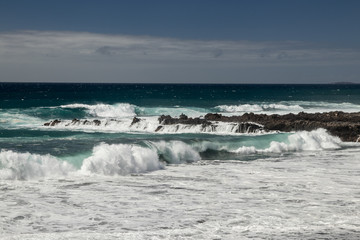 Fototapeta premium Steep high lava rock cliffs. Blue sea horizon, natural sky background.