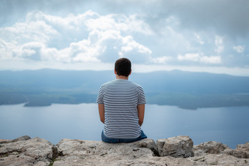 man sitting on a rock and looking at the sea