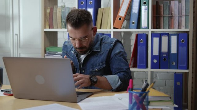Busy hesitating young hipster man working first day doubting dropping things trying to get things done staying in office company.