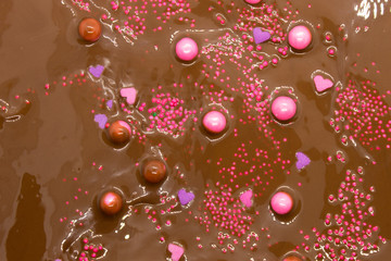 This is a photograph of Milk chocolate topped with round and heart shaped Pink and Purple sprinkles