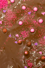 This is a photograph of Milk chocolate topped with round and heart shaped Pink and Purple sprinkles