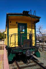 Fototapeta na wymiar Yellow and green railway caboose sits on the rails waiting for the next tourist to ride in