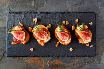 Crostini appetizers with figs, brie cheese and walnuts. Above view on a slate serving platter.