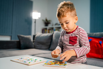 Small boy little playing at home alone by the table with puzzle developing mental skill having fun learning