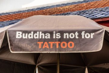 Obraz premium Bangkok city, Thailand - March 17, 2019: Tattoo statement of Buddha printed on patio umbrella at Temple of Dawn, with black and red roof on top.