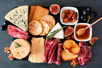 Cheese board with a selection of cheeses and meats. Top view on a dark slate background.