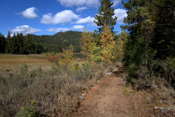 Hiking trail around a mountain lake in the early days of autumn with colors starting to appear with blue cloudy skys overhead.
