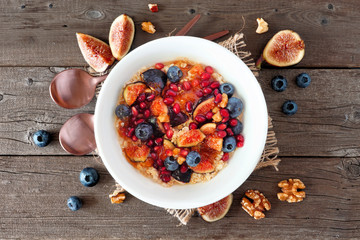 Bowl of oatmeal with figs, blueberries, pomegranates and sweet jelly. Above view on a wood background with frame of ingredients. Autumn food concept.