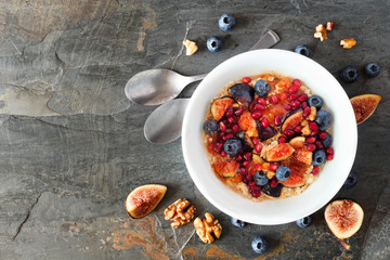 Oatmeal with figs, blueberries, pomegranates and sweet jam. Top view on a slate background with copy space. Fall food concept.