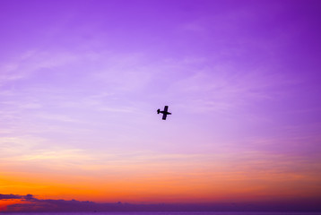 A silhouette shot of a small plane shot against the setting sun. The sky is lit brightly and overlooks a tranquil ocean