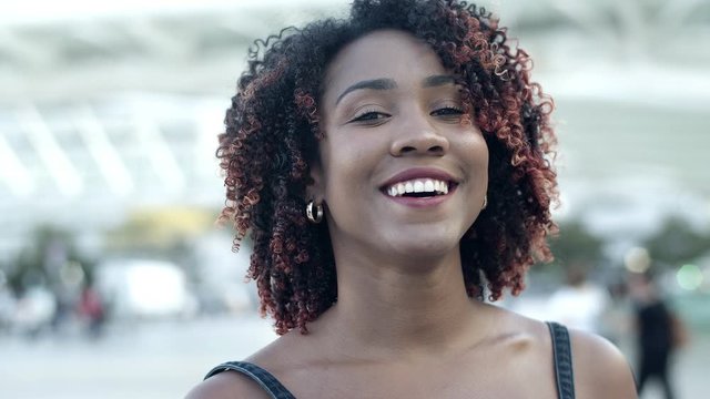 Front view of smiling curly lady standing on street. Closeup shot of smiling woman posing outdoors. Female beauty concept