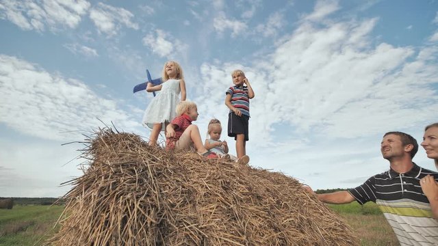 Children launch airplanes while standing on a stack of straw in front of their parents.