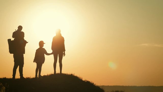 Parents and two children walking in the mountains at the sunset time. Silhouette happy beautiful family during the travelling. Concept of friendly family and travel.