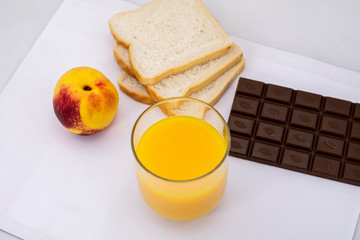 Breakfast consisting of natural orange juice, ripe peach, white bread and milk chocolate
