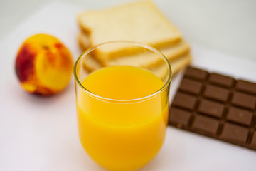 Breakfast consisting of natural orange juice, ripe peach, white bread and milk chocolate