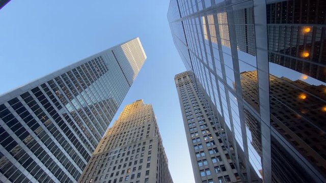 An extreme wide shot looking up at tall Manhattan office buildings on a clear summer blue sky day. Slow dolly move.  	