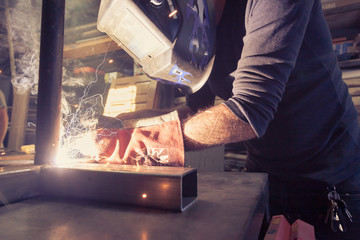 Welder with full face mask and thick gloves leans forward for precise welding joints