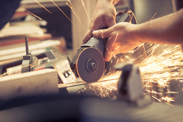 Pair of hands awkwardly holding a grinder power tool and cutting metal, throwing sparks everywhere