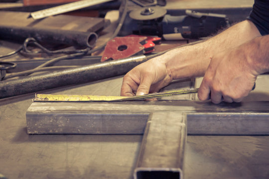 A weathered pair of hands takes measurements of some metal bars with a measuring tape
