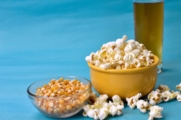 popcorn inside bowl with pink bottom with corn beside on blue background