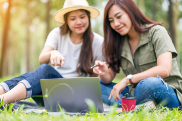 Two asian women working and using laptop computer while sitting in the park