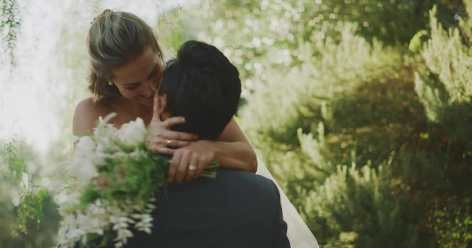 Happy multi ethnic groom spinning his bride in his arms on their wedding day, smiling diverse couple embracing and kissing in nature
