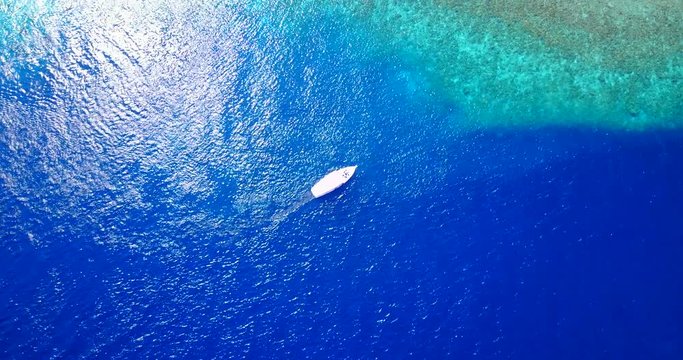 Aerial top down rotating view around a sailing boat, over colorful ocean surface reflecting sunlight near Cerralvo island