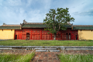 Fototapeta na wymiar Oriental red monument in Imperial City, Hue. Famous gallery behind tall grass moving by wind breeze. Ruins in Citadel famous landmark of Vietnam.