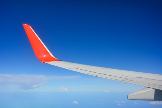 red wing of the aircraft view from airplane window seat flying in the blue sky with white clouds background, copy space