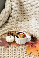 Fototapeta na wymiar Spiced cider with orange and cinnamon on woven tray with maple fall leaves, pinecones, and pumpkin, cozy chunky knit blanket