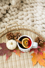 Spiced cider with orange and cinnamon on woven tray with maple fall leaves, pinecones, and pumpkin, cozy chunky knit blanket
