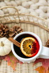 Spiced cider with orange and cinnamon on woven tray with maple fall leaves, pinecones, and pumpkin, cozy chunky knit blanket