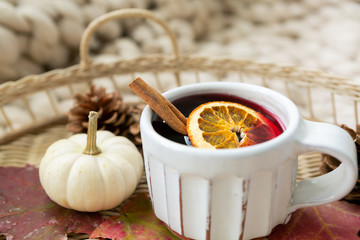 Spiced cider with orange and cinnamon on woven tray with maple fall leaves, pinecones, and pumpkin, cozy chunky knit blanket