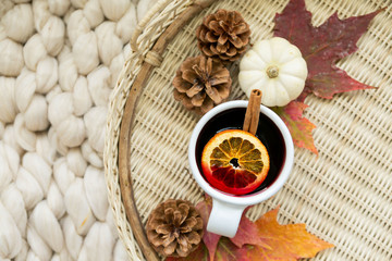 Spiced cider with orange and cinnamon on woven tray with maple fall leaves, pinecones, and pumpkin,...