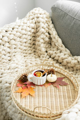 Spiced cider with orange and cinnamon on woven tray with maple fall leaves, pinecones, and pumpkin, cozy chunky knit blanket
