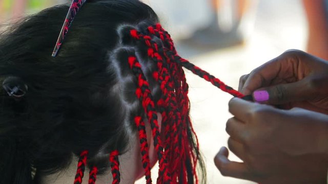 A dark-skinned girl braids an braid to a red-haired brunette woman