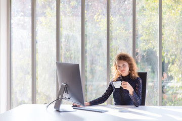 A business woman has a smiling and bright face, sipping coffee in the morning in her office with a...