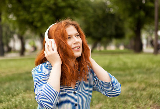 Red-haired beautiful girl in white headphones. Red-haired girl listens to music.