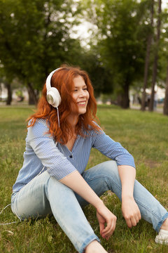 Red-haired beautiful girl in white headphones. Red-haired girl listens to music.