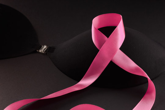 Pink ribbon on a black bra against a dark background to support a breast mammary cancer awareness campaign in october.