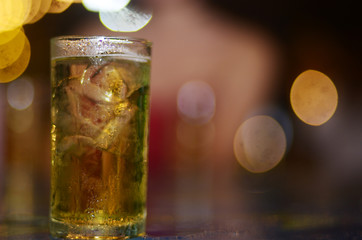 A glass of yellow beverage from the fermentation of beer and Ice on the table and with bokeh