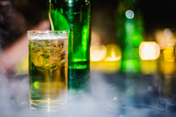 A glass of yellow beverage from the fermentation of beer and Ice on the table and with bokeh
